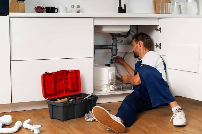 Emergency plumbing technician on floor with red toolbox performing repairs
