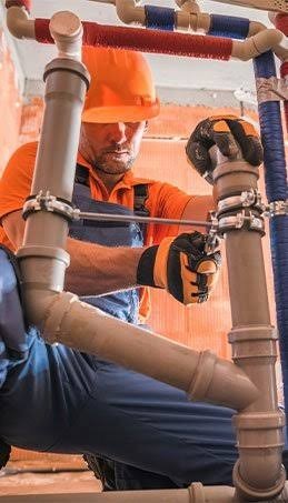 Commercial plumber installing overhead pipes with metal vibration clamps