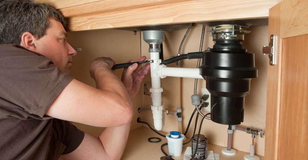 Master plumber tightening kitchen sink disposal and P-trap drain lines