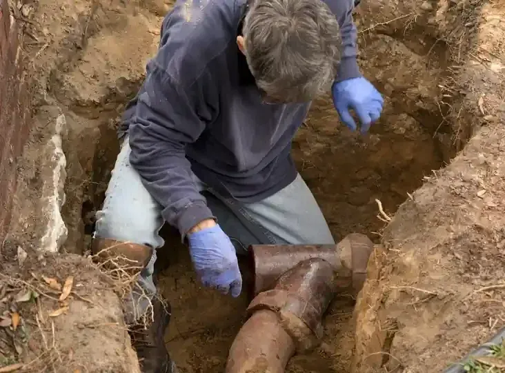 Master plumber repairing underground sewer lateral pipe in excavated trench